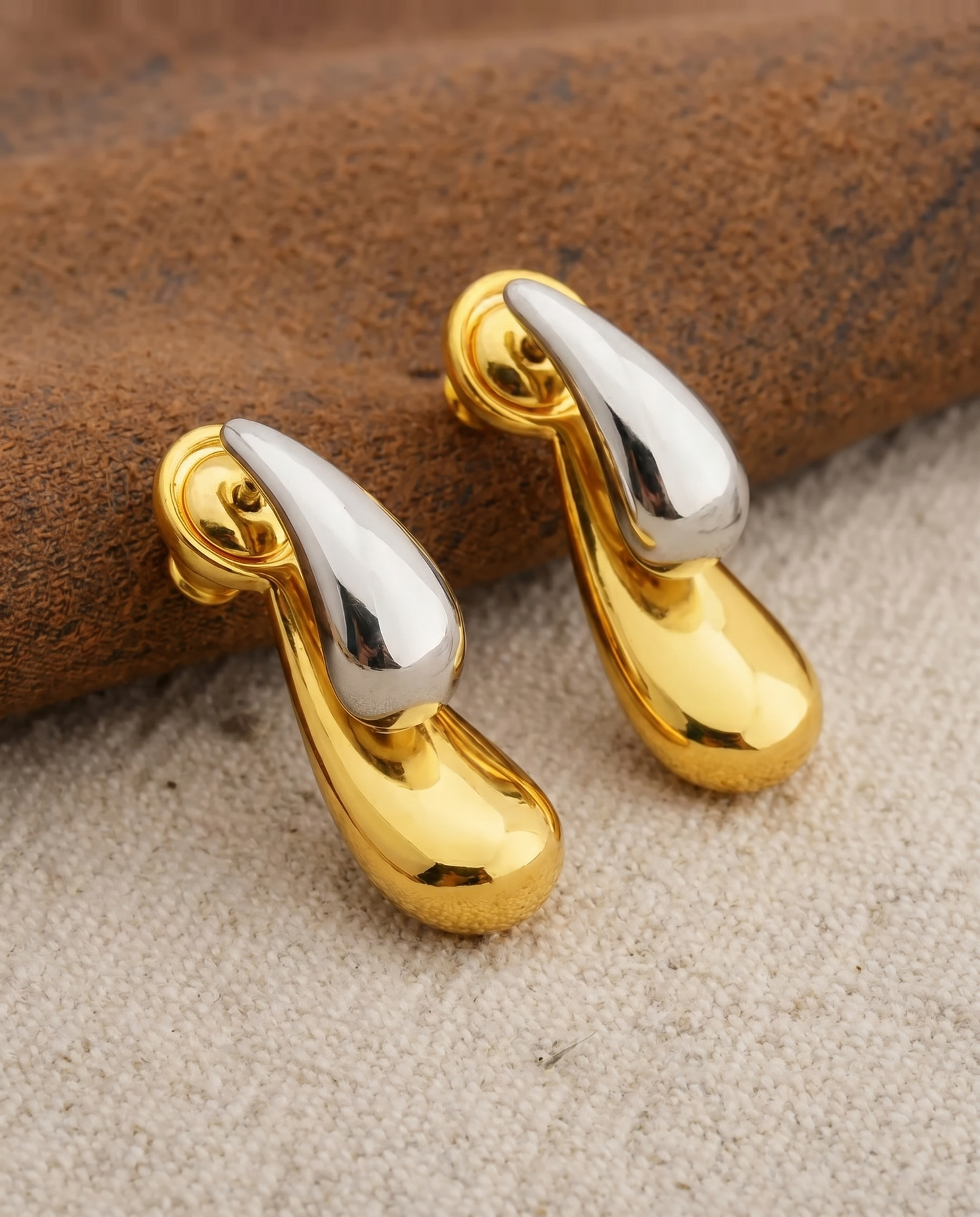 Gold and silver teardrop-shaped earrings on a textured surface
