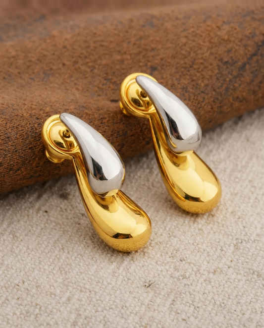 Gold and silver teardrop-shaped earrings on a textured surface